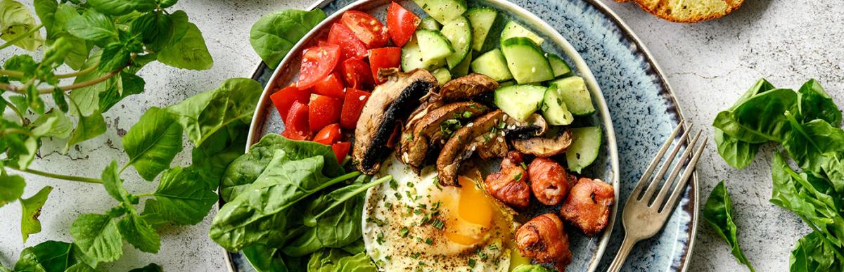 Plate of healthy breakfast options, sliced avocado, eggs, grilled mushrooms, sliced cucumbers and spinach