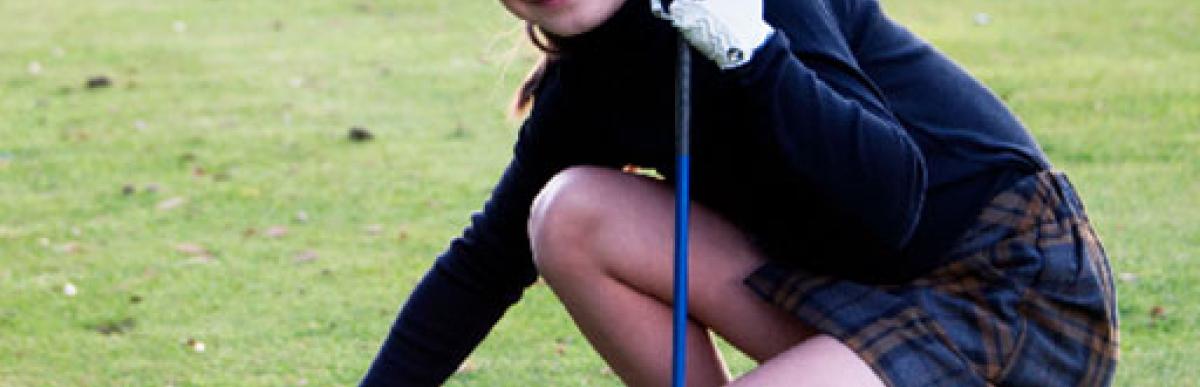 Smiling young girl setting a golf ball on a tee.
