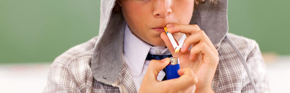 School teen boy lighting cigarette in classroom